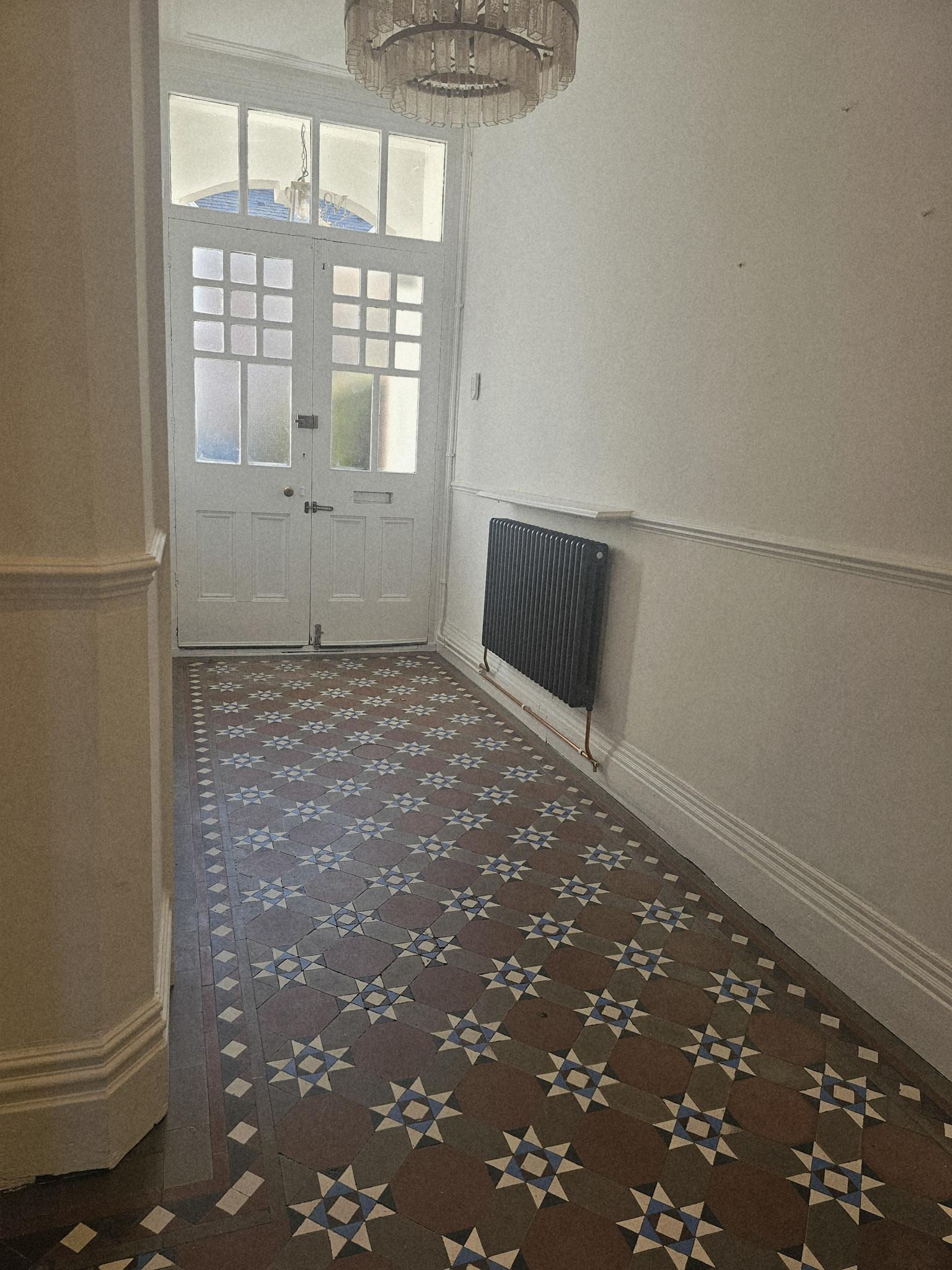 Hallway before restyling: an empty corridor with a patterned tiled floor, white walls and a radiator by the front door.
